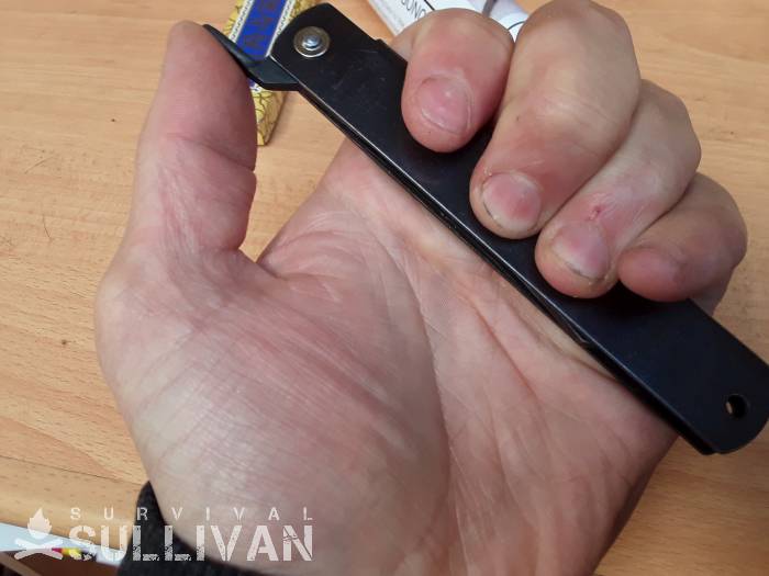 Thumb resting on the tang of the Higonokami knife