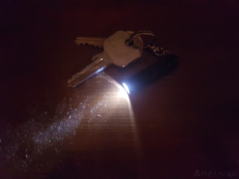 a small keychain flashlight lit in the dark next to some keys