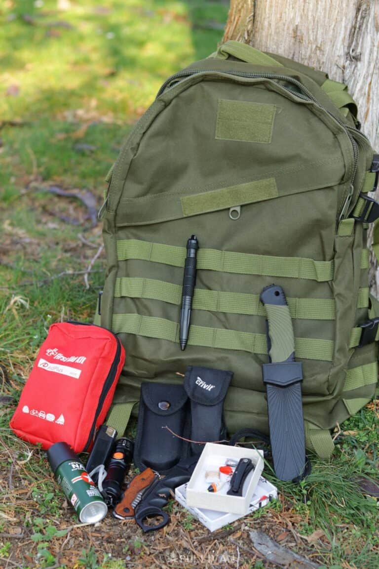 green molle bug out bag with first aid kit, knife, multi-tool, and fishing kit, next to it