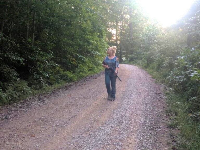 woman holding a rifle in the middle of a country road