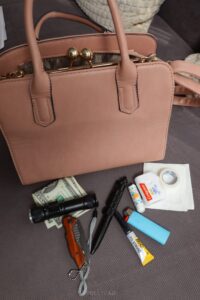 flashlight, tactical pen, folding knife, and more next to pink purse