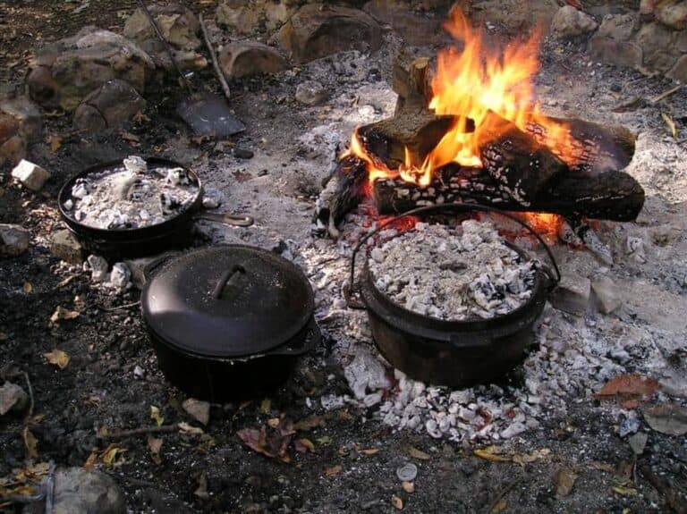 cast iron Dutch oven and cast iron skillet next to open outdoor fire