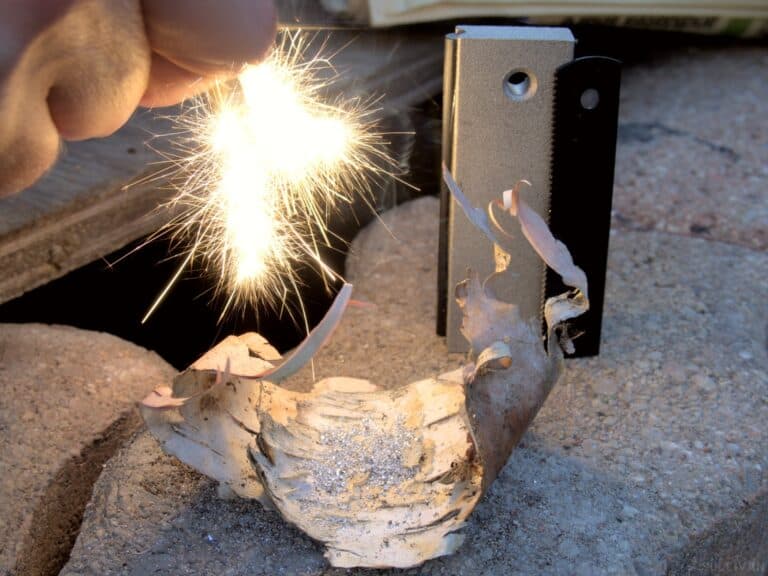 using a ferro rod to ignite magnesium shavings block and striker behind the birch bark